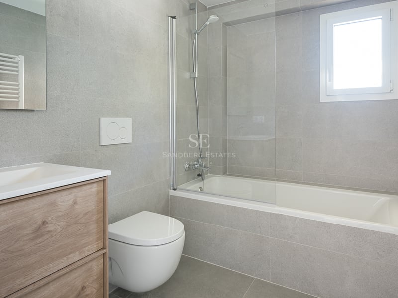 Salle de bain contemporaine avec carrelage gris effet pierre, baignoire et paroi en verre, et meuble sous vasque en chêne.