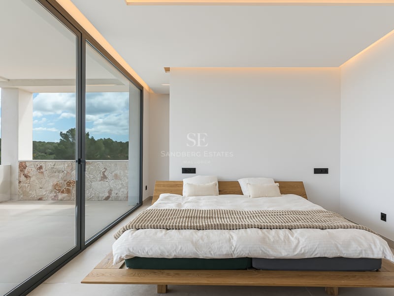 Minimalistisches Schlafzimmer mit Holzbett, großen Glasschiebetüren und Zugang zum Balkon mit Natursteinmauer.