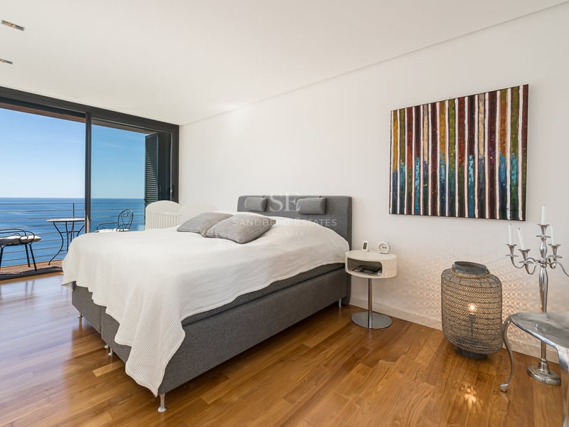 Modern bedroom featuring oak floors and floor-to-ceiling glass doors opening to a Mediterranean sea view.