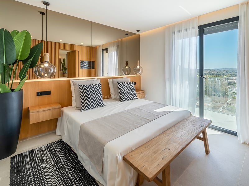 Chambre contemporaine avec tête de lit en chêne, mur miroir et grandes baies vitrées ouvrant sur le paysage.