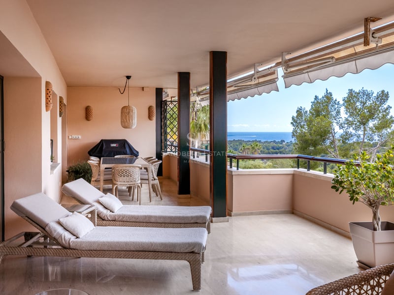 Terrasse couverte avec bains de soleil, salle à manger extérieure et vue sur la mer et la verdure.