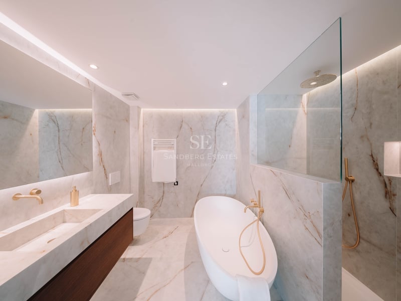 Salle de bain moderne en marbre avec baignoire îlot blanche, robinetterie dorée et double vasque.