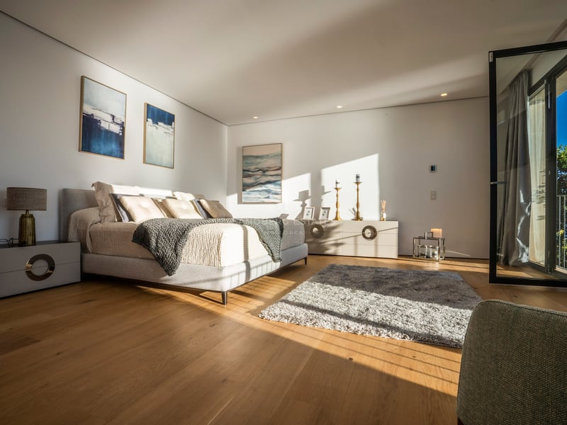 Modernes Schlafzimmer mit großem Bett, hellem Eichenboden, Balkontür und intensivem natürlichem Lichteinfall.