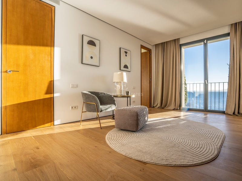 Modernes Zimmer mit Eichenparkett, grauem Sessel und Glastüren mit Blick auf das Mittelmeer.