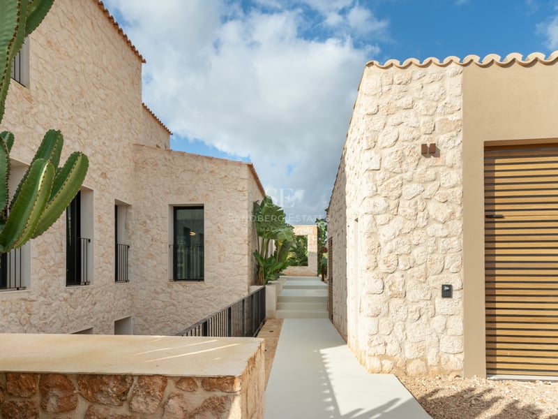 Minimalistisk naturstensgång mellan två samtida villabyggnader under en klarblå himmel.