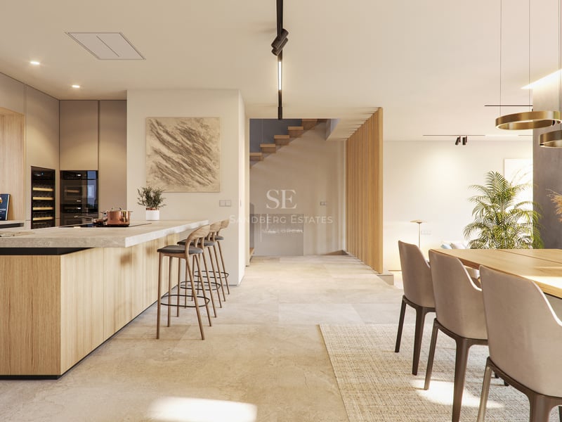 Interior view of a contemporary open-plan kitchen with light wood cabinetry, stone floors, and a breakfast bar.