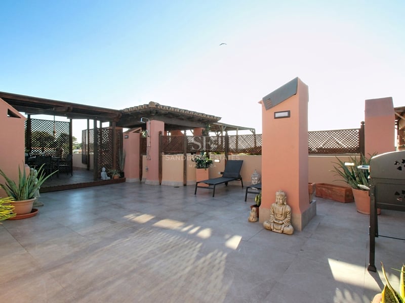 Medelhavstak-terrass med terrakotta-väggar, träpergola, stengolv och solstolar under en klarblå himmel.