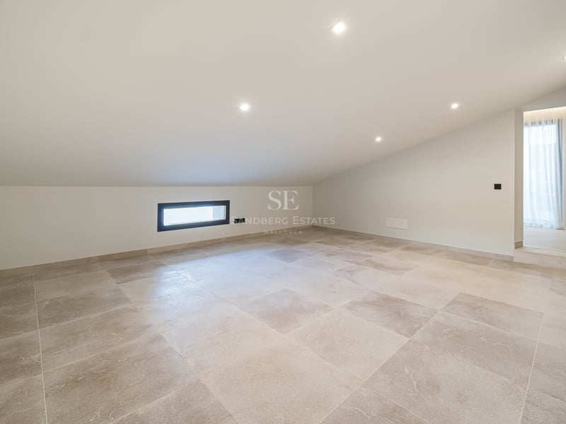 Pièce vide avec plafond incliné blanc, carrelage en pierre beige et spots encastrés.