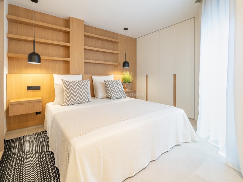 Chambre moderne avec tête de lit en chêne intégrée, étagères, literie blanche et armoires encastrées blanches.