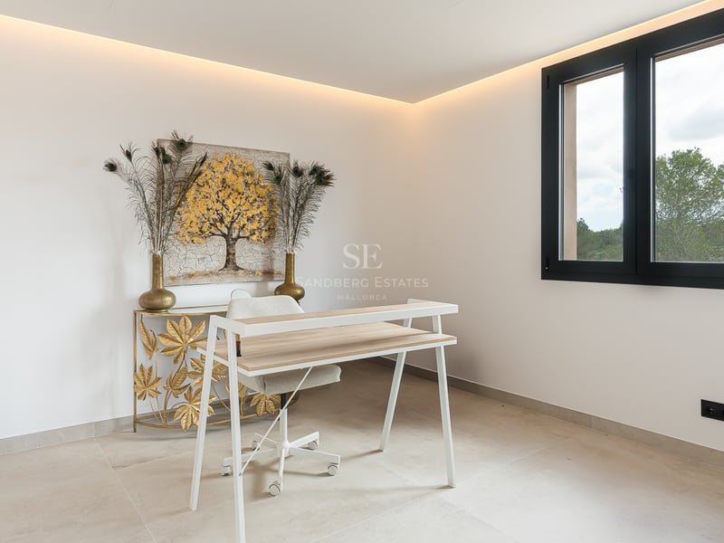 Ein moderner Arbeitsbereich mit weißem Schreibtisch, goldenem Kunstwerk und indirekter LED-Deckenbeleuchtung.