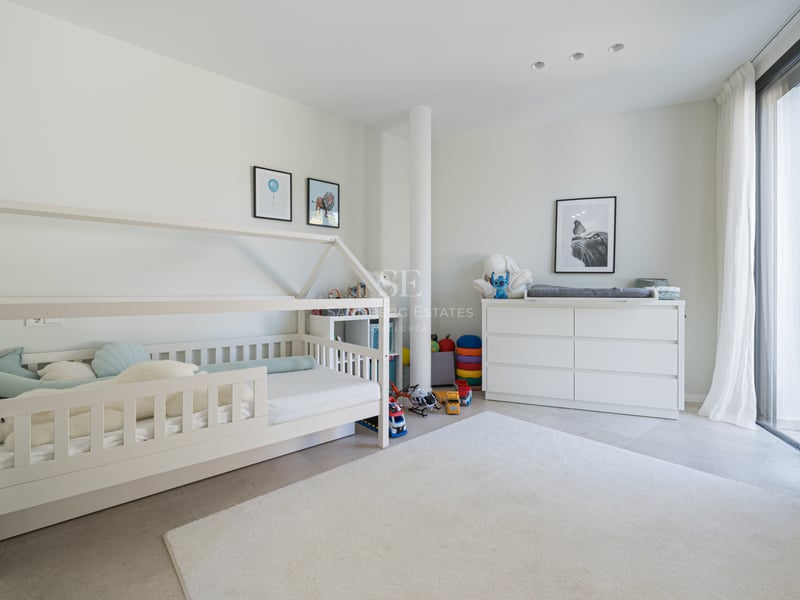 Chambre d'enfant moderne avec lit cabane blanc, commode et grandes baies vitrées avec voilages.