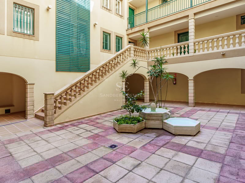 Innergård med schackrutigt golv, stenfontän, storslagen trappa med balustrad och klassiska valv.