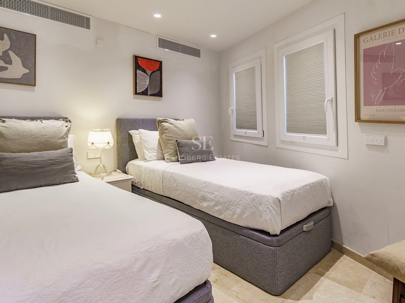 Bedroom with two single beds, grey headboards, white linens, and contemporary wall art.