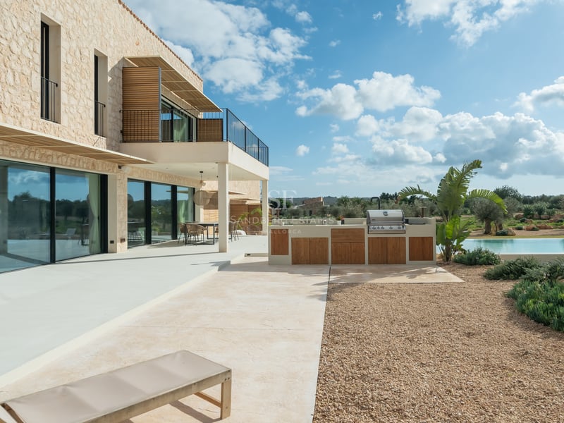Modern terrass med utomhuskök i trä, naturstensfasad och stora fönsterpartier.