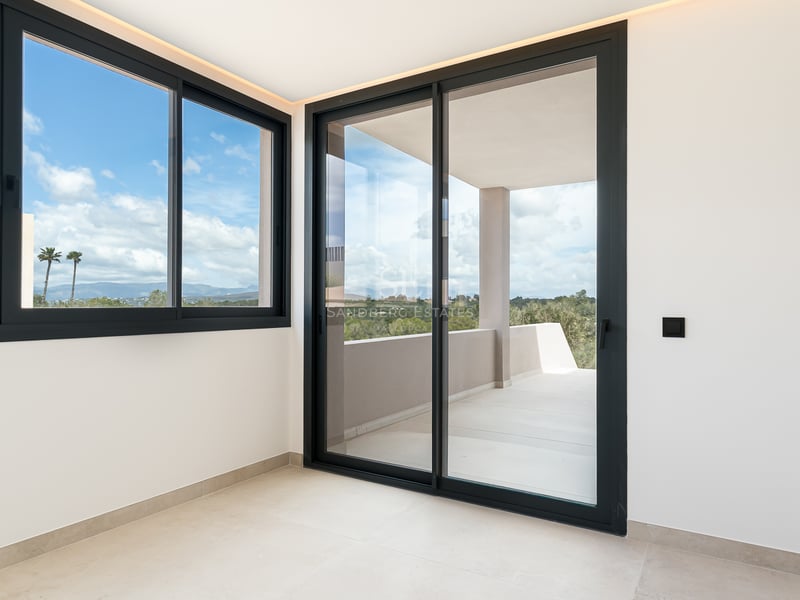 Heller moderner Raum mit großen Schiebefenstern mit schwarzem Rahmen, die auf eine sonnige private Terrasse führen.