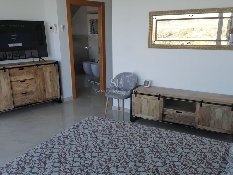 Chambre moderne avec consoles en bois rustique, grand téléviseur et vue sur la salle de bain privée.