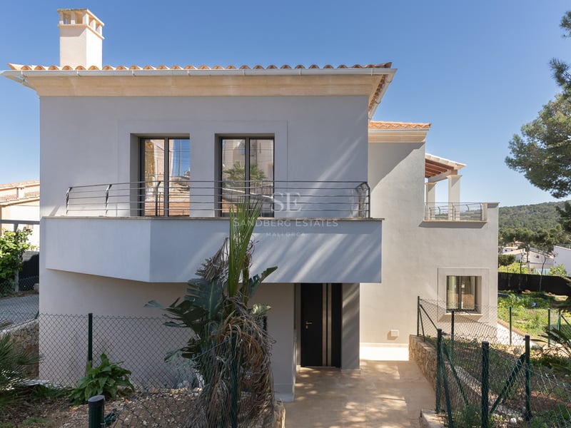 Tvåvånings modern villa med vit fasad, takpannor i terrakotta och balkong under en klarblå himmel.