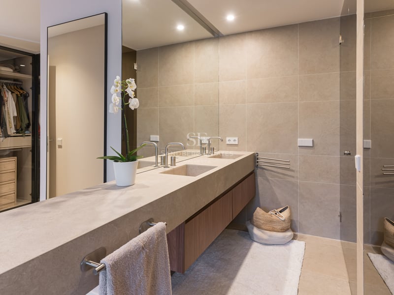 Modern bathroom featuring double stone vanity, large mirror, and glass-enclosed walk-in closet with internal lighting.