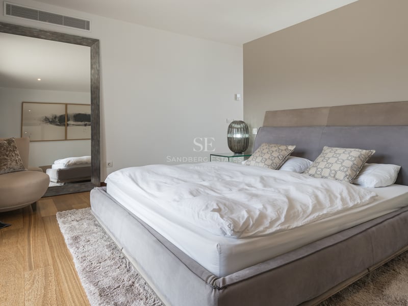 Chambre moderne avec lit gris rembourré, parquet en chêne, grand miroir au sol et tables de chevet en verre.