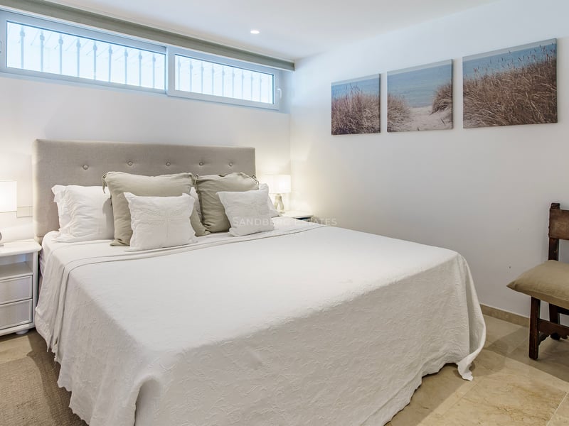 A bright bedroom featuring a large bed with a tufted headboard, white bedding, and coastal artwork on the wall.