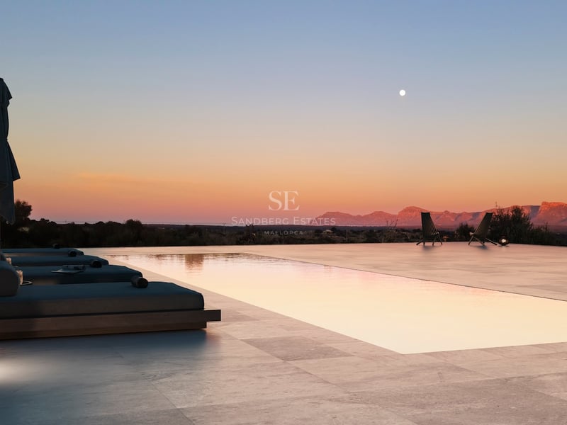 Piscine à débordement et terrasse en pierre au crépuscule surplombant des montagnes sous un ciel de coucher de soleil.