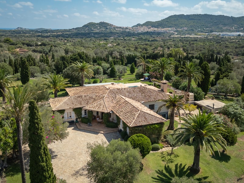 Vue aérienne d'une villa méditerranéenne aux toits de tuiles, entourée de palmiers et d'un vaste jardin paysager.