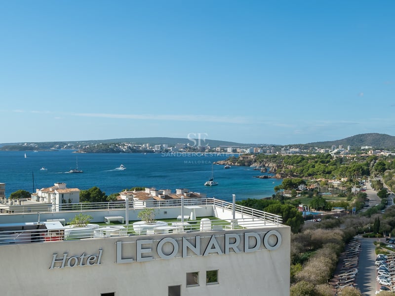 Panoramic view of a Mediterranean bay and coastline from a modern rooftop terrace with white railings and artificial turf.