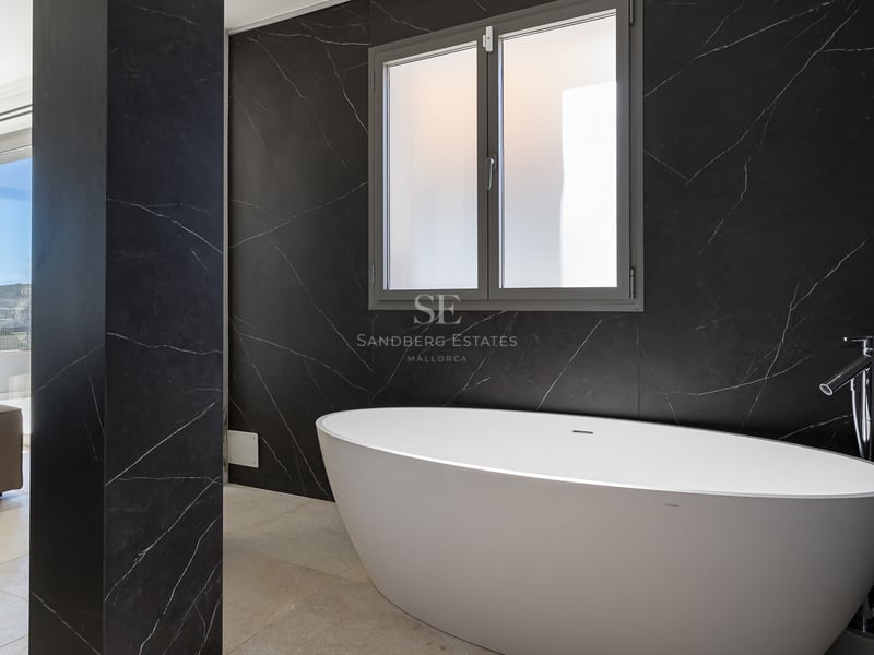 Ett modernt badrum med ett vitt ovalt fristående badkar mot en svart marmorvägg och ett frostat fönster.