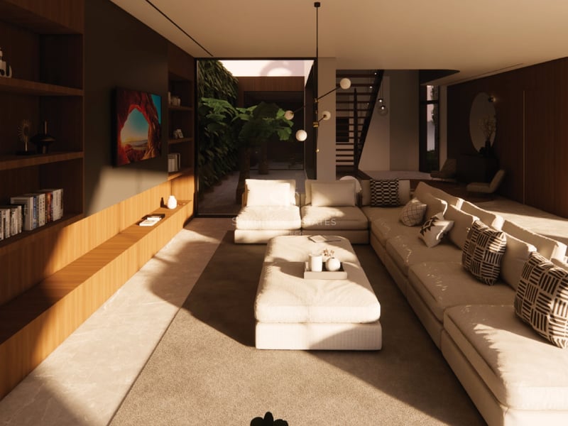 Salon moderne avec grand canapé crème, bibliothèque en bois intégrée et patio intérieur avec végétation.