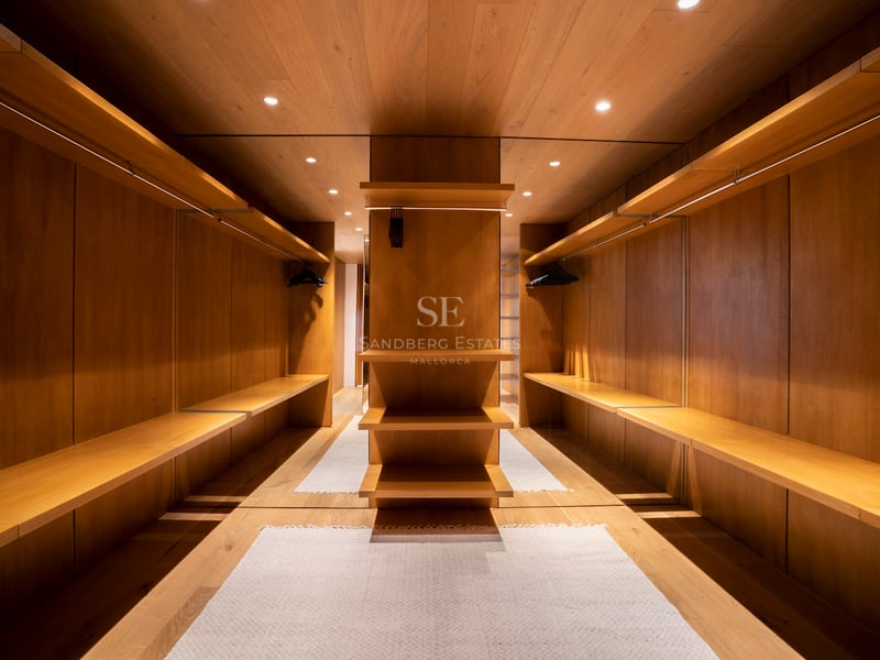 Symmetrischer begehbarer Kleiderschrank mit Eichenpaneelen, offenen Regalen und warmer LED-Beleuchtung.