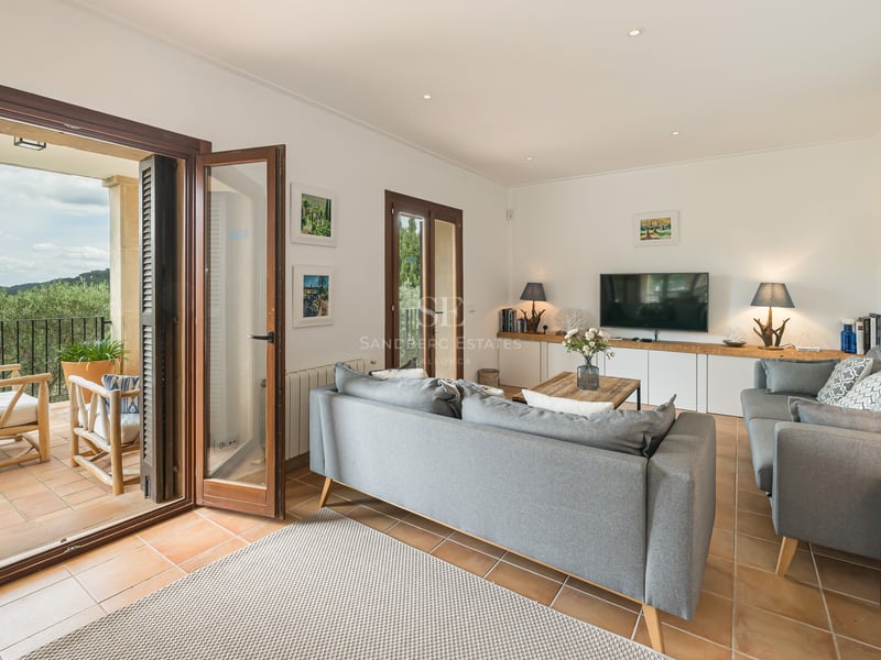Canapé gris moderne dans un salon avec sol en terre cuite et portes-fenêtres ouvrant sur une terrasse.