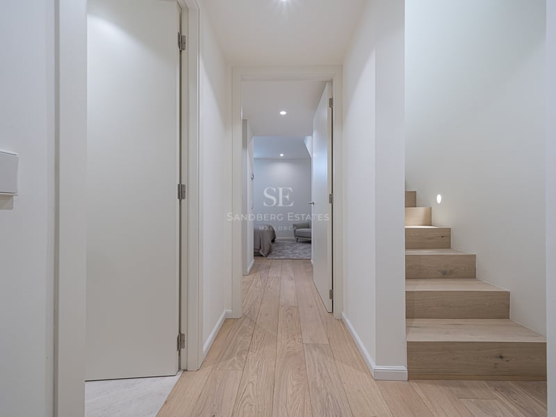 Modern hallway featuring light oak wood floors, white doors, and a minimalist wooden staircase.