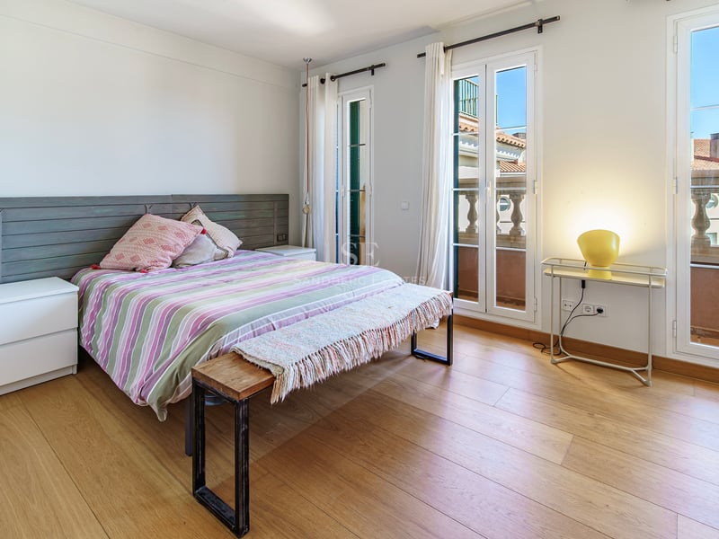 Ljust sovrum med ekparkett, dubbelsäng och altandörrar som leder ut till en klassisk balkong.