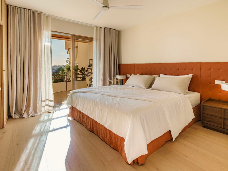 Geräumiges modernes Schlafzimmer mit orangefarbenem Kopfteil, Holzboden und Glasschiebetür zu einer sonnigen Terrasse.