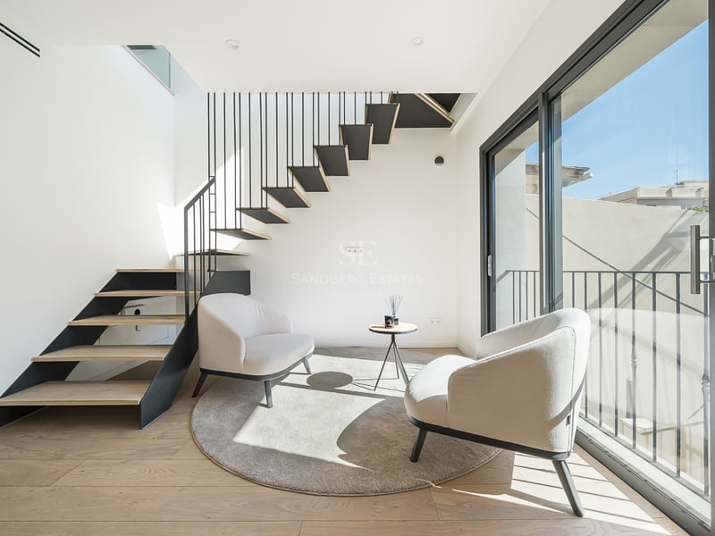 Bright room featuring two cream armchairs, a round rug, and a modern wood and metal staircase by a glass door.