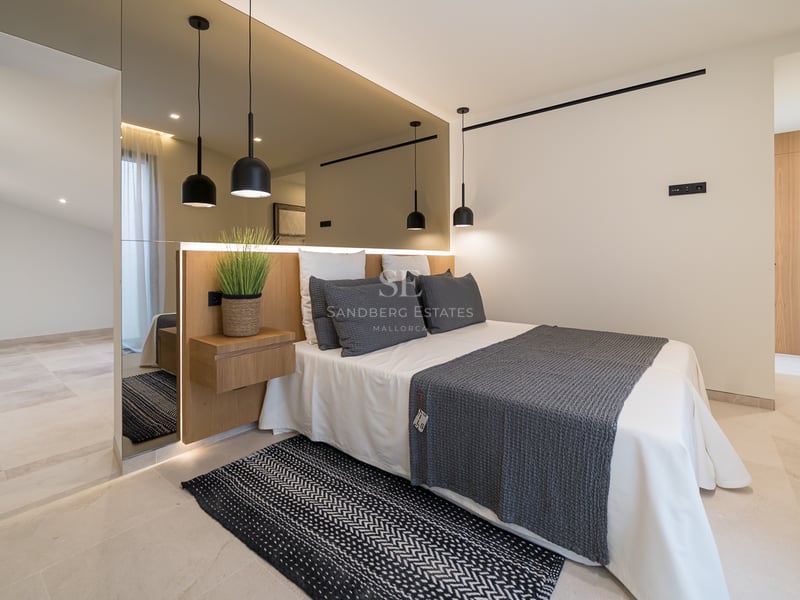 Chambre moderne avec un grand mur de miroirs derrière le lit, suspensions noires et sol en pierre claire.