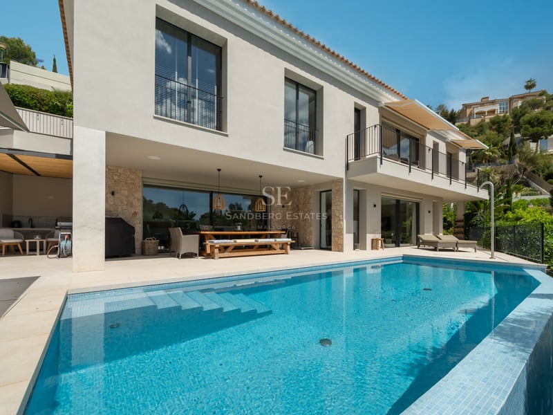 Vue piscine turquoise, jardin luxuriant, architecture moderne, façade blanche, larges fenêtres, reflets de lumière, ciel bleu.