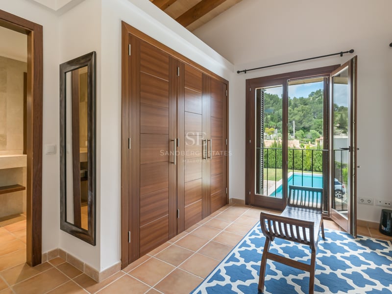 Chambre lumineuse avec grands placards en bois, sol en terre cuite et vue sur une piscine.