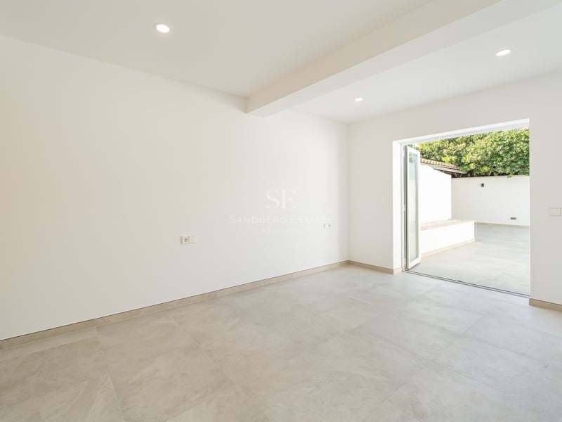 Pièce lumineuse et vide avec sol gris, murs blancs, placard en bois et porte vitrée donnant sur un patio.