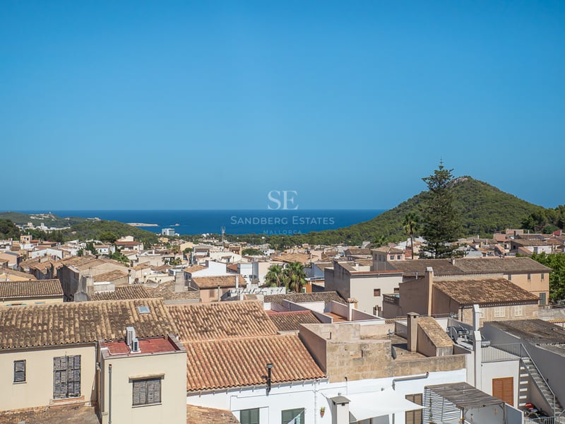 Vue surélevée de toits en terre cuite traditionnels menant à la mer Méditerranée et à une colline verdoyante.