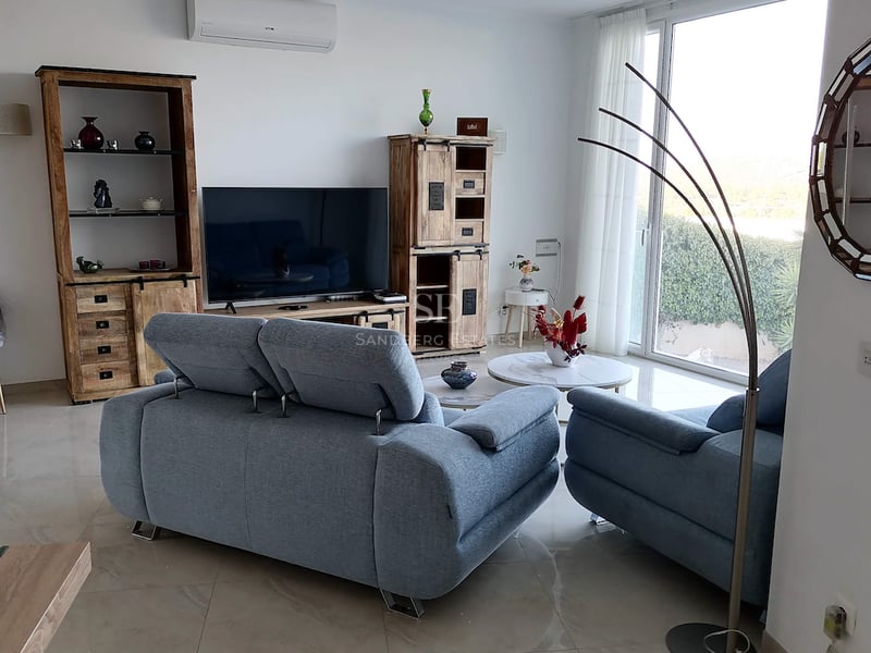 Salon moderne avec canapés bleus, meubles en bois massif, sol en grès cérame poli et grande baie vitrée.