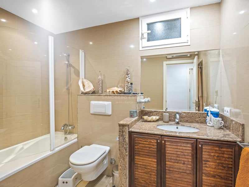 Badezimmer mit Badewanne, Glaswand, dunklem Holz-Waschtisch, Granitplatte und sandfarbenen Fliesen.