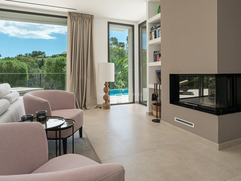 Salon lumineux avec grandes baies vitrées offrant une vue sur la mer. Intérieur moderne avec canapé beige, table basse et détails décoratifs élégants.