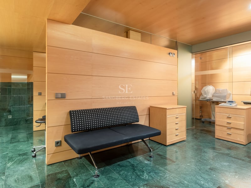 Intérieur avec sol en marbre vert, boiseries claires, banc noir et équipement de consultation médicale.