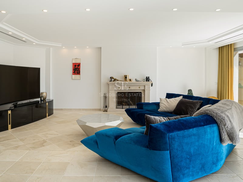 Moderner Wohnbereich mit blauem Samtsofa, Steinkamin und Natursteinboden unter LED-Einbaustrahlern.