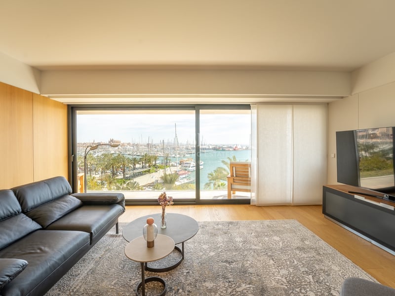 Modernt vardagsrum med svart lädersoffa framför stora glaspartier som visar en hamn fylld med båtar.