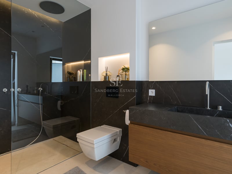 Salle de bain moderne avec murs en marbre noir, toilettes suspendues, vanité en bois et douche à l'italienne vitrée.