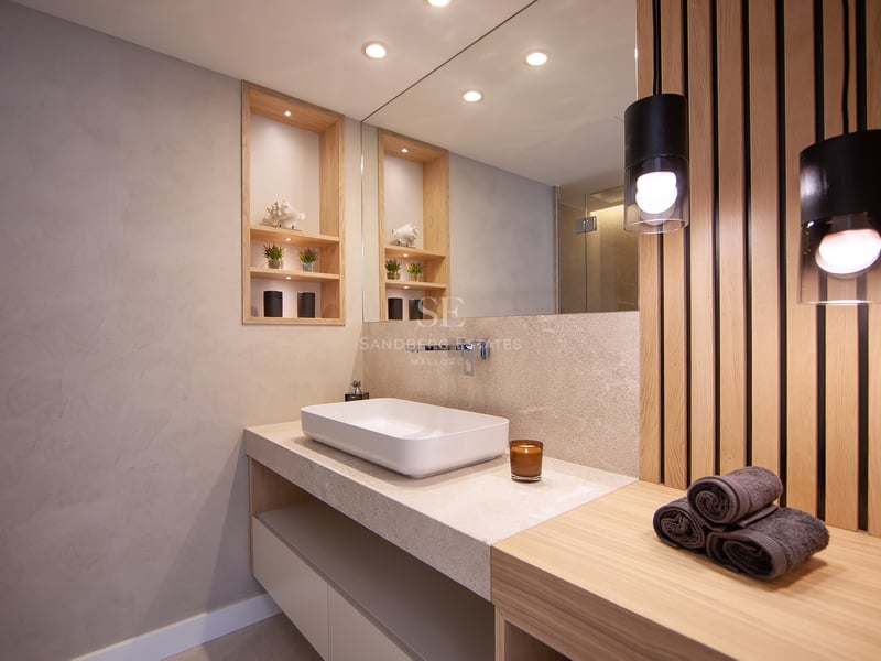 Salle de bain moderne avec vasque à poser, plan de travail en pierre, mur en lattes de bois et éclairage chaleureux.