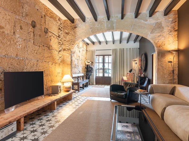 Salon moderne avec murs en pierre d'origine, arche, poutres apparentes et carrelage hydraulique traditionnel.