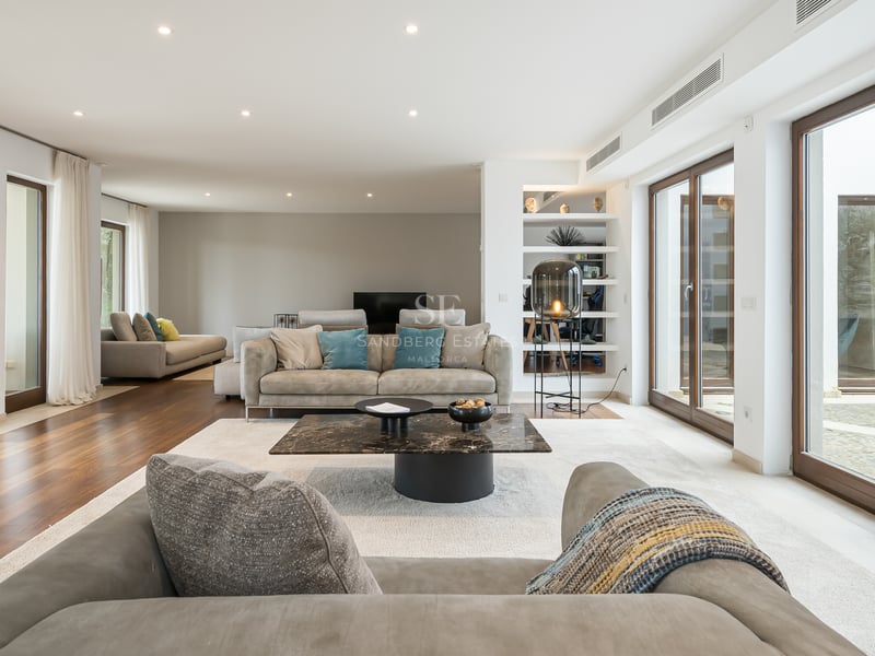 Grand salon moderne avec parquet, canapés gris contemporains, table basse en marbre et grandes baies vitrées.